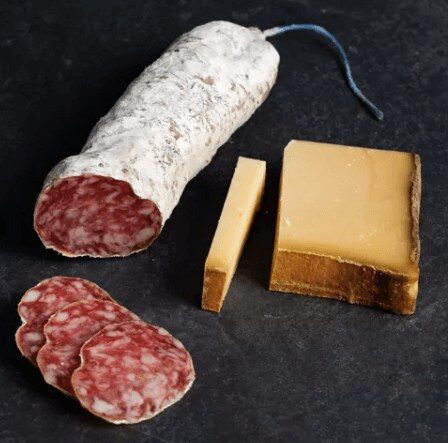 Un saucisson sec pur porc au Beaufort AOP tranché à côté d’un morceau de beaufort