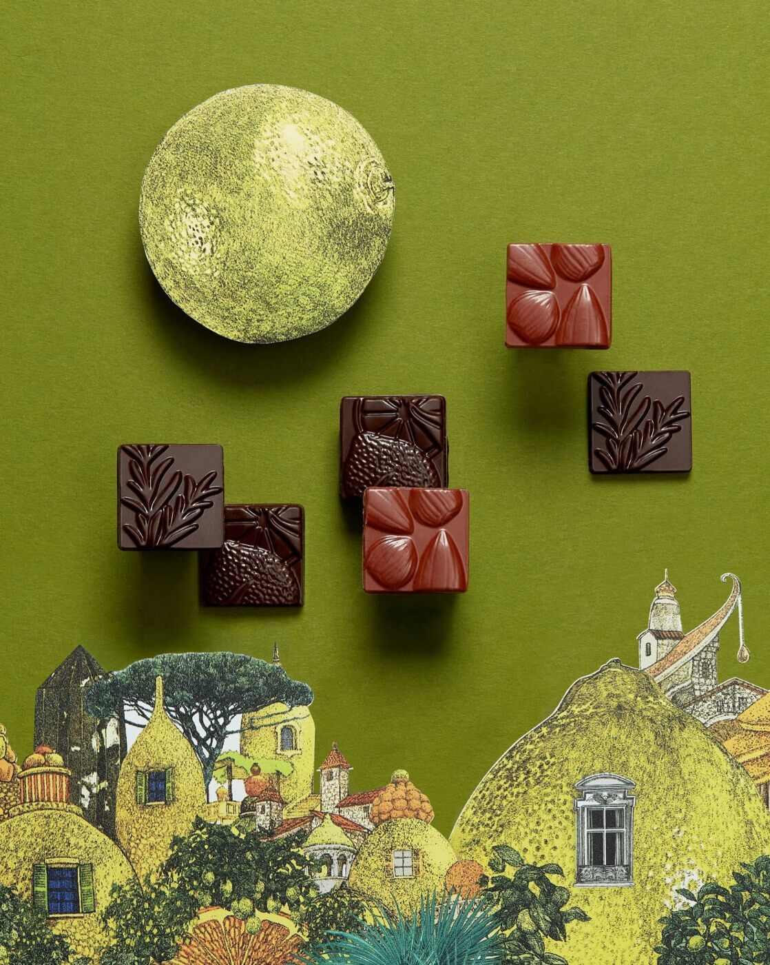 Les carrés fourrés au chocolat de l’Avant-Avent Alain Ducasse sur un fond vert illustré d’un village provençal