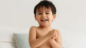 Petit garçon souriant assis sur un lit en couche Biolane