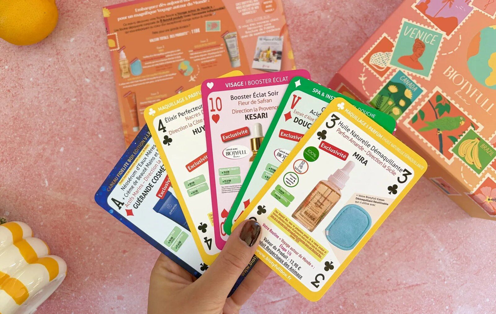 Les fiches produits de la Biotyfull Box Voyage autour du Monde tenues en éventail devant la boîte