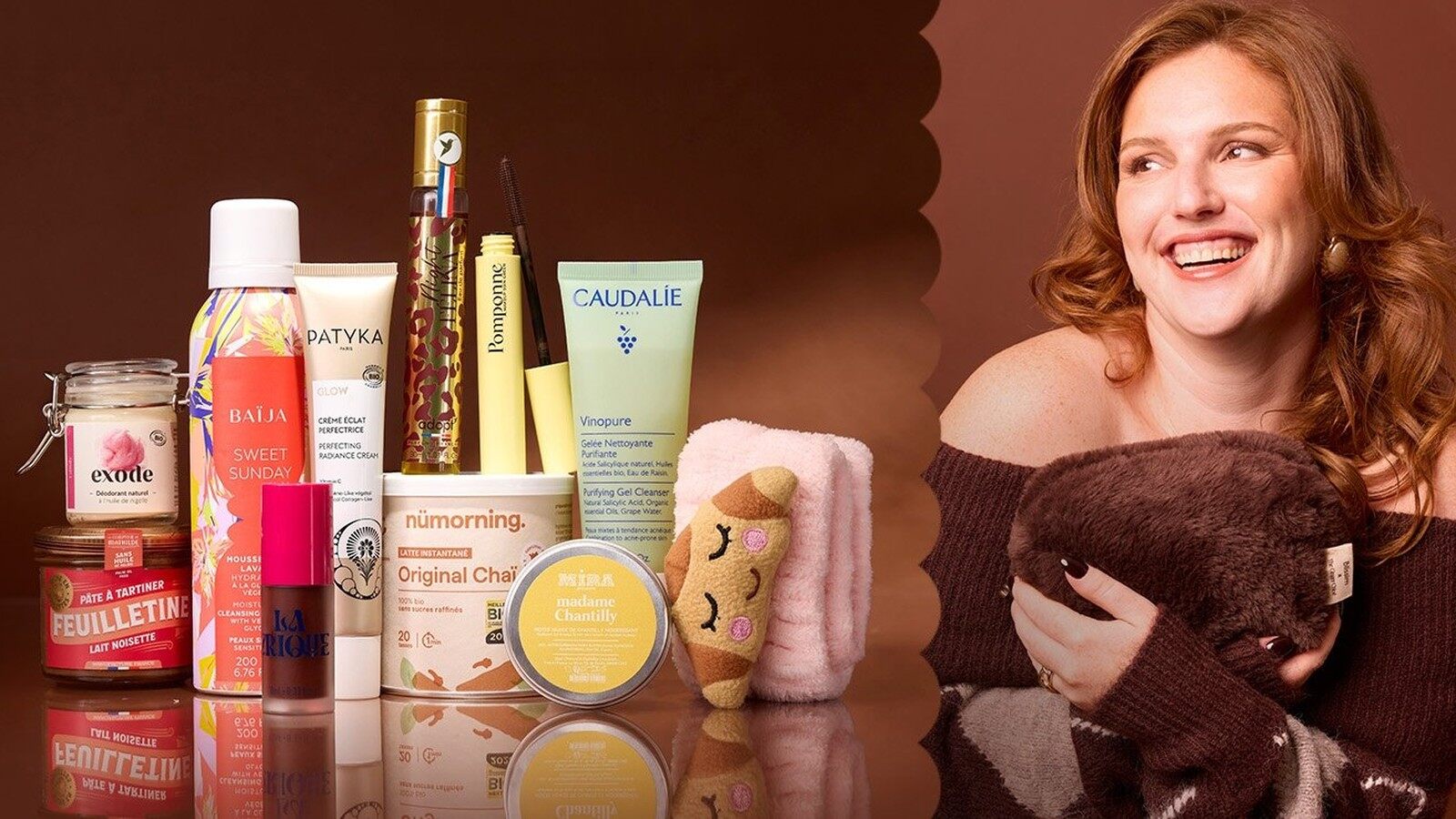 TheGingerChloé sourit avec une trousse en fausse fourrure à côté des produits de son édition Blissim