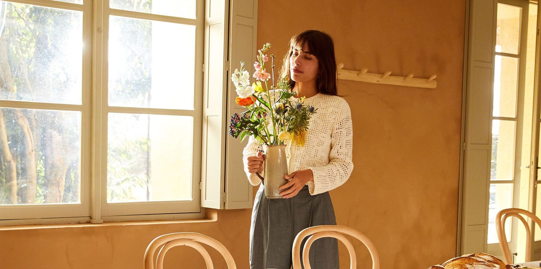 Une jeune femme dans un salon lumineux arrange un bouquet de fleurs des champs dans un vase en céramique