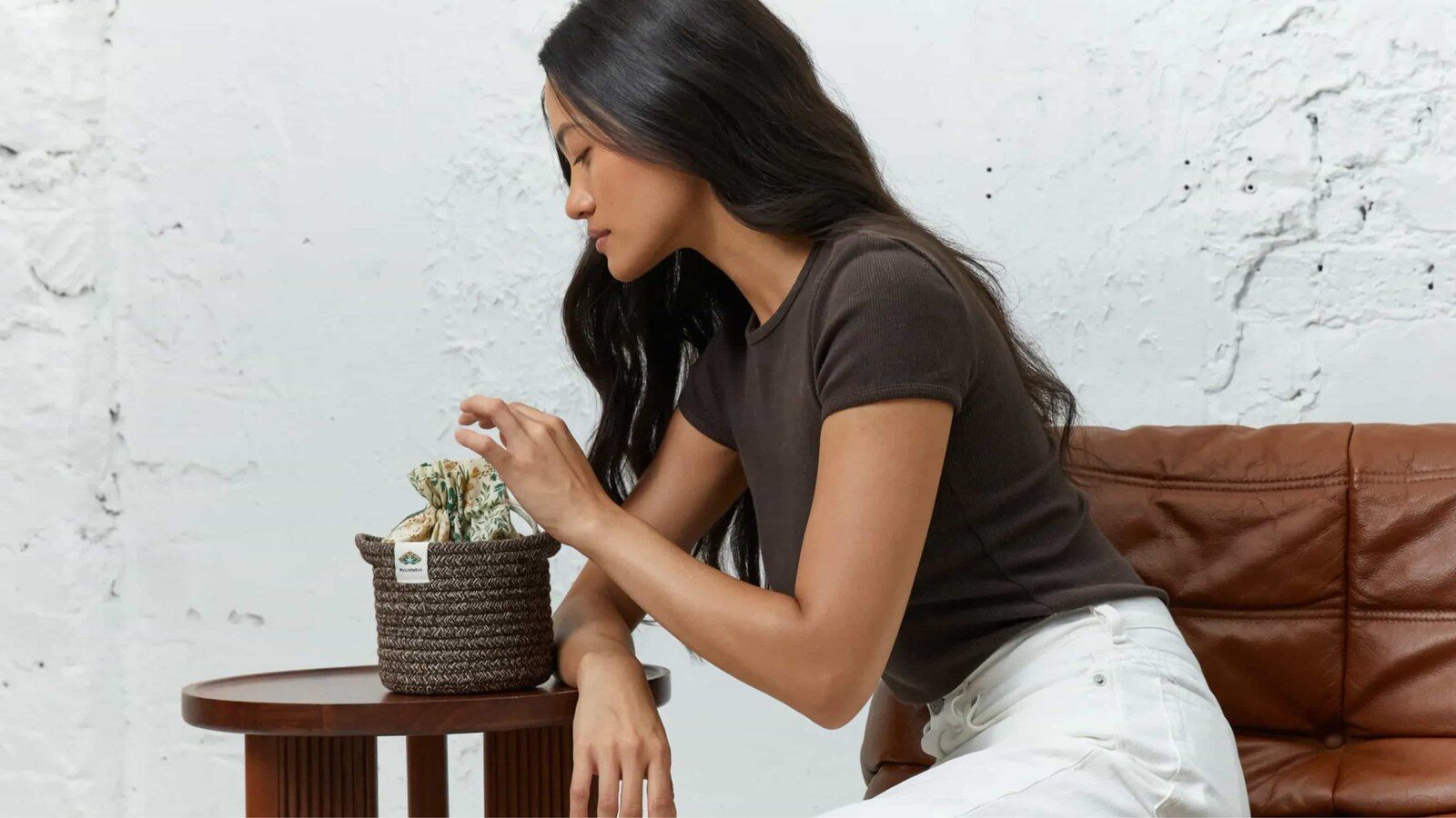 Une jeune femme assise près d’une table basse découvre un petit panier tressé rempli de surprises My Little Box