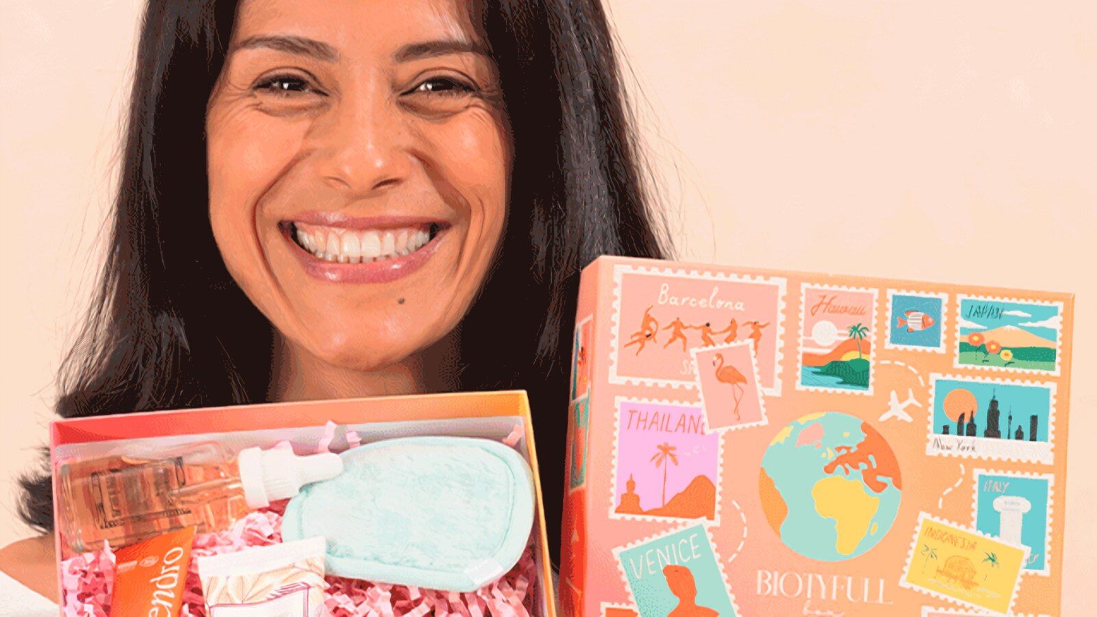 Une femme souriante présente une box Biotyfull ouverte remplie de soins et le coffret Voyage autour du Monde