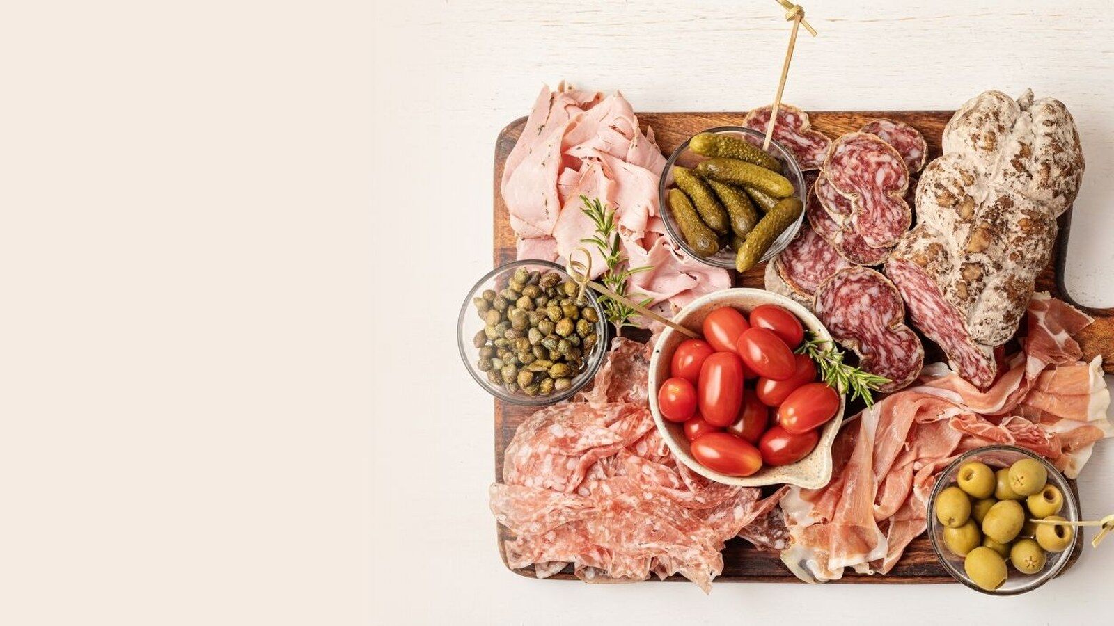 Une planche apéro garnie de charcuteries, tomates cerises, cornichons, olives et câpres