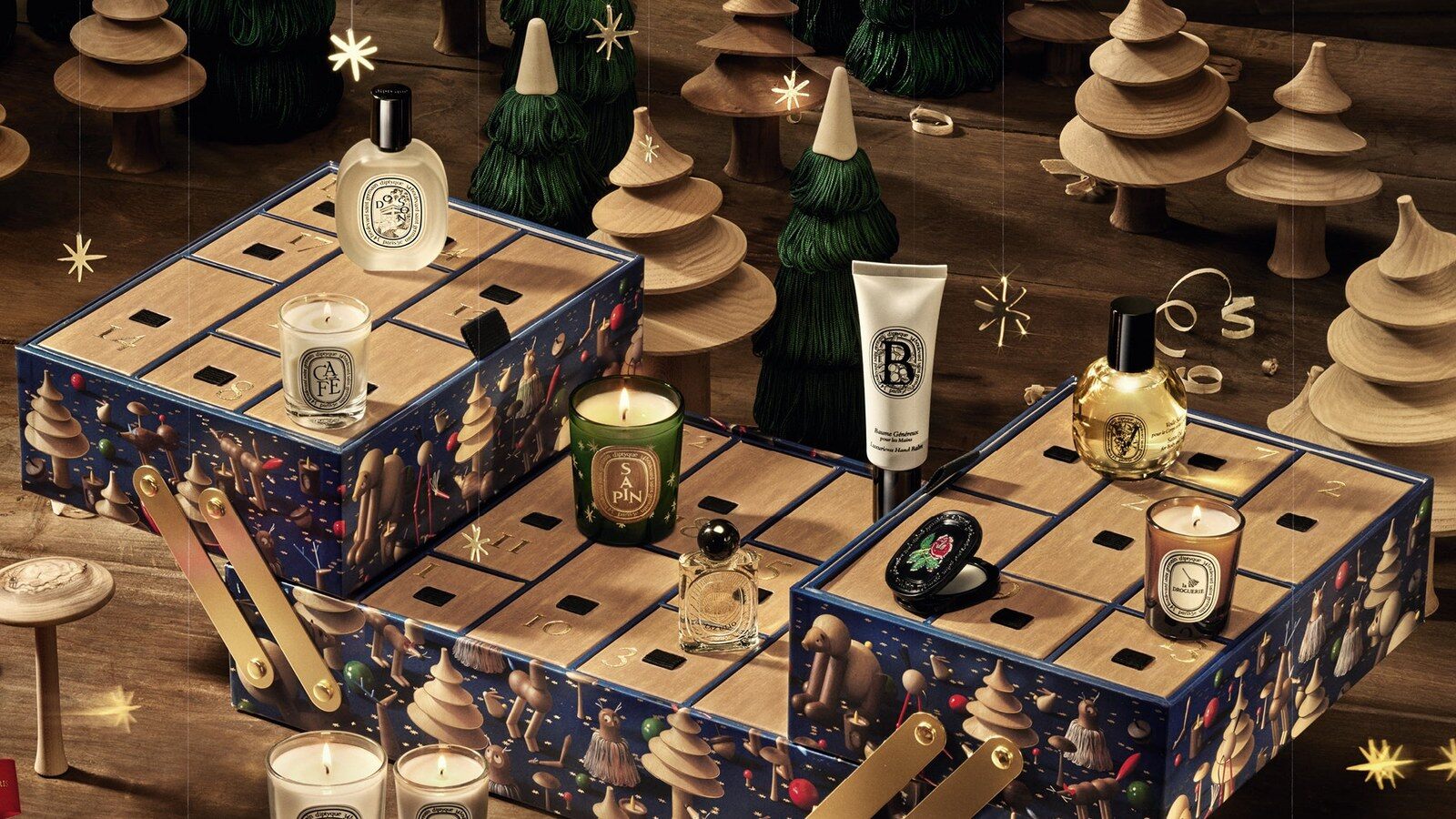 Le calendrier de l’Avent Diptyque 2026 aux tiroirs ouverts, entouré de bougies et de petits sapins en bois tourné