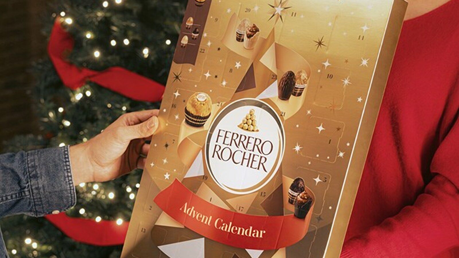 Deux personnes se passent le calendrier de l’Avent Ferrero Rocher devant un sapin de Noël illuminé