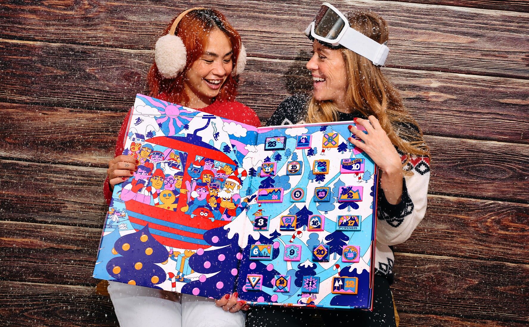 Deux amies en tenue de ski tenant le grand calendrier de l’Avent Noël à ski 2026 du Chocolat des Français ouvert