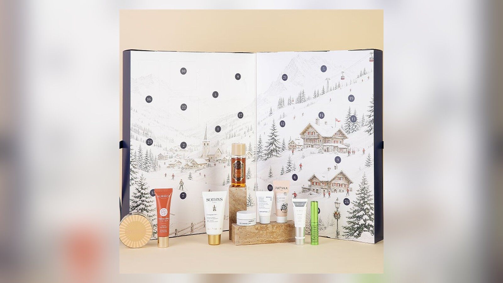 Le calendrier de l’Avent Marie Claire 2026 ouvert sur un décor de village de montagne enneigé, avec plusieurs de ses soins posés devant