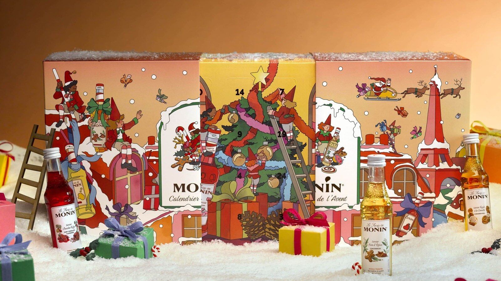 Le calendrier de l’Avent Monin 2026, un coffret illustré de lutins et de la tour Eiffel, entouré de mini-bouteilles de sirop sur de la neige