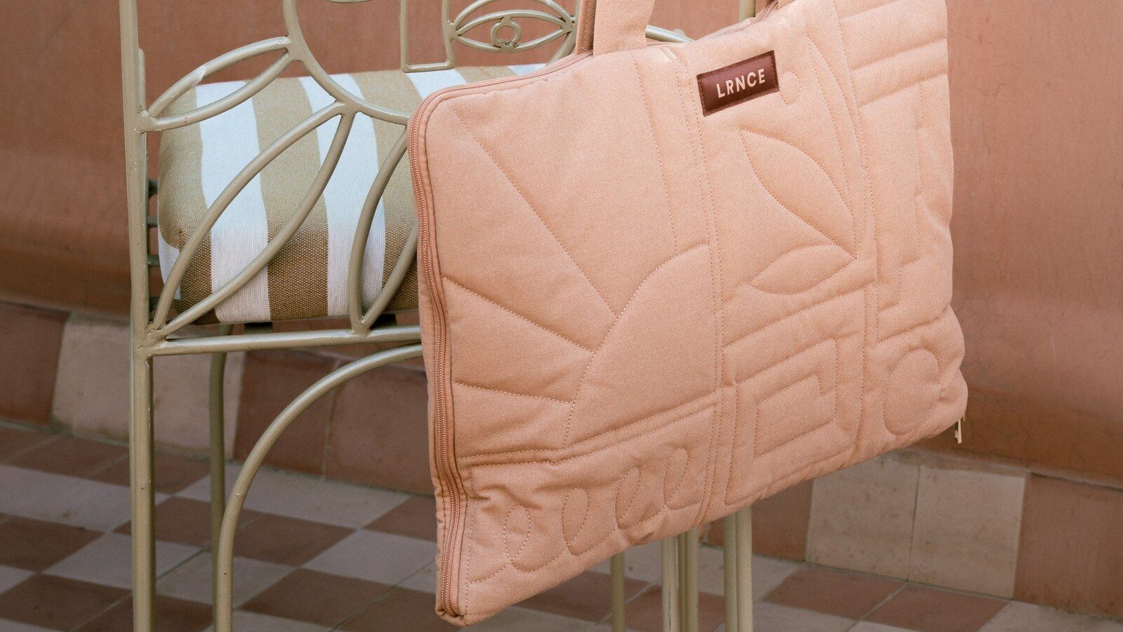 La pochette matelassée rose du calendrier de l’Avent Oh My Cream x LRNCE 2026 portée en sac, suspendue à une chaise en fer forgé