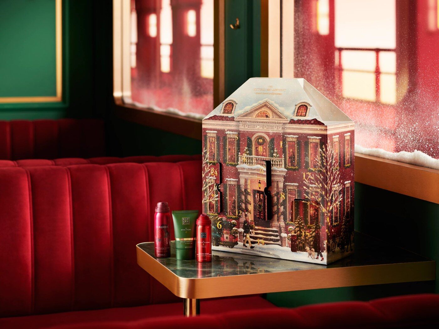 Le calendrier de l’Avent Rituals Classic 2026 en forme de maison illustrée, posé sur une table dans un wagon de train rouge et vert