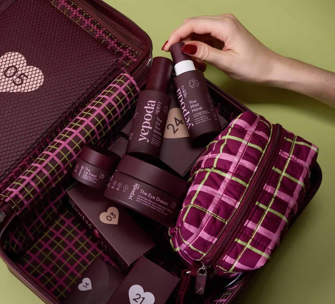 Le calendrier de l’Avent Yepoda 2026 : une valise bordeaux ouverte, une trousse à carreaux roses et des soins Yepoda sur fond rouge