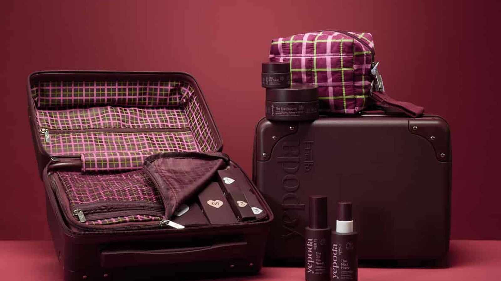 La valise bordeaux du calendrier de l’Avent Yepoda 2026 ouverte à côté d’une trousse à carreaux roses et de soins Yepoda, sur fond rouge