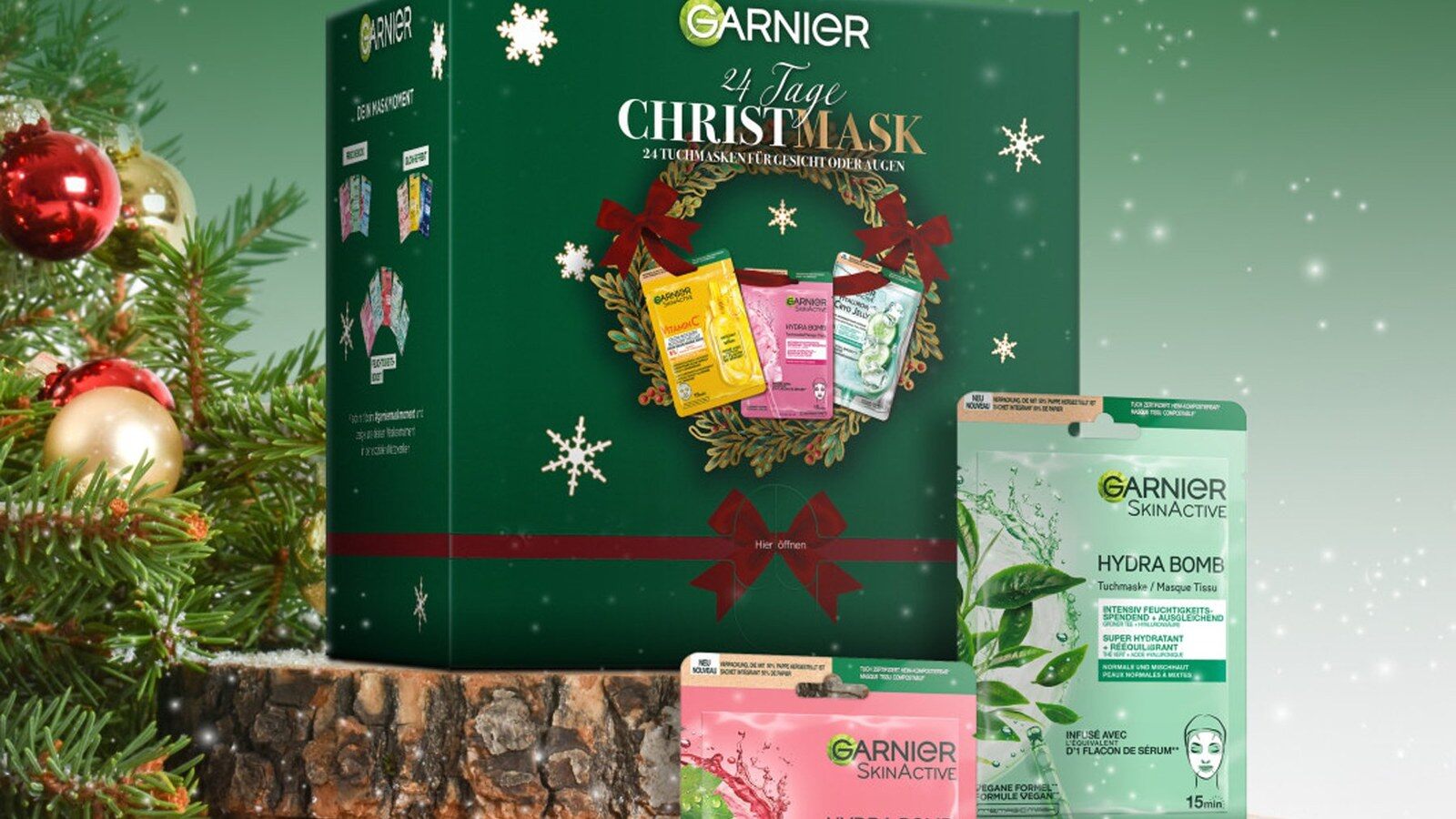 Le calendrier de l’Avent Garnier posé sur des rondins de bois dans un décor de Noël enneigé, avec des masques en tissu