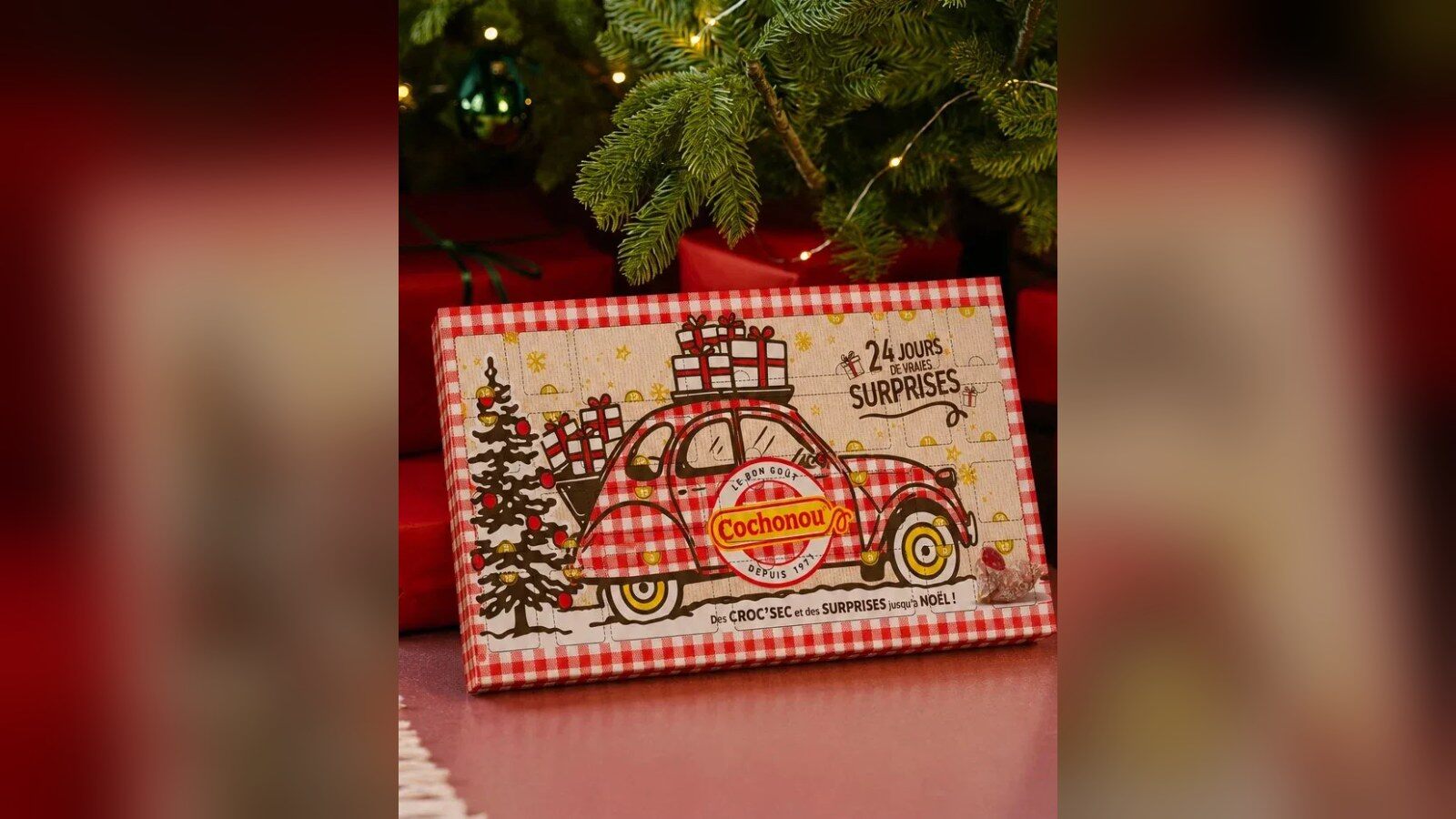 Le calendrier de l’Avent Cochonou à carreaux vichy, avec une 2 CV chargée de cadeaux, posé devant un sapin