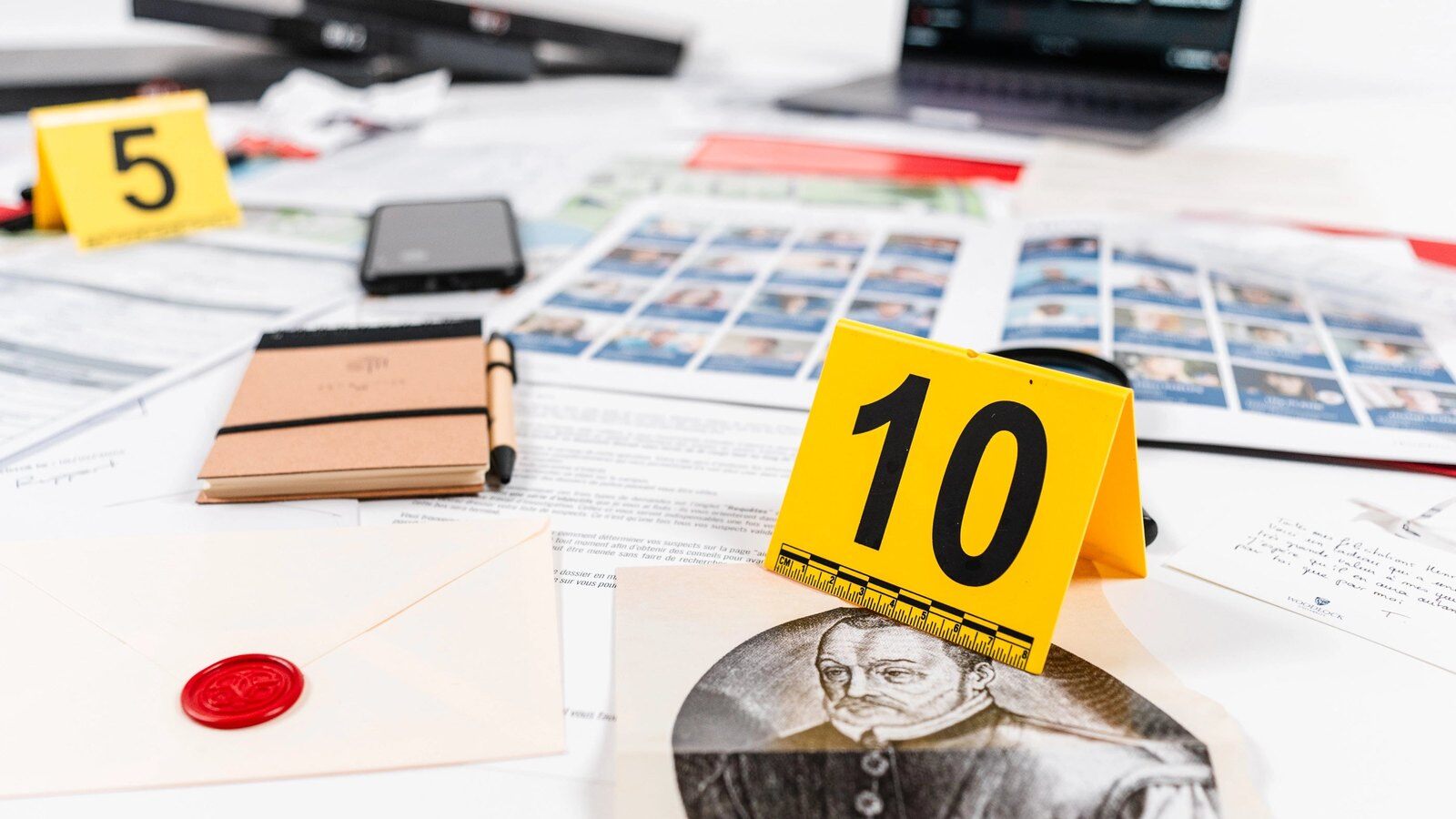 Pièces à conviction d’une enquête Detective Box étalées sur une table, avec marqueurs jaunes numérotés et enveloppe scellée