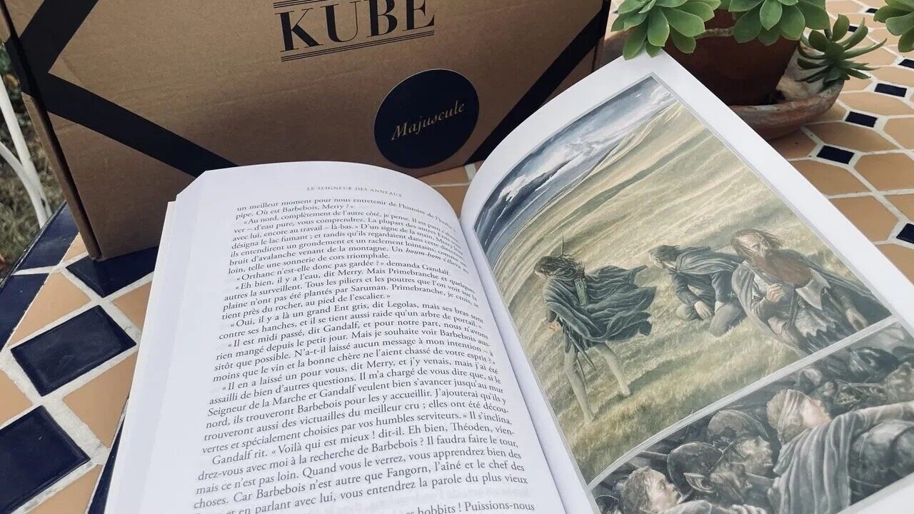 Un livre illustré ouvert devant une box Kube Majuscule sur une table en mosaïque