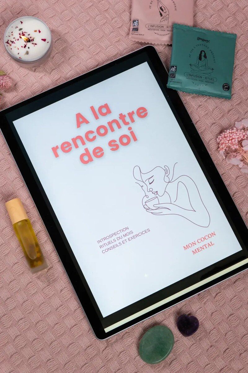Une tablette affiche l’e-book « À la rencontre de soi » de Mon Cocon Mental, entourée d’une bougie, d’infusions et de pierres