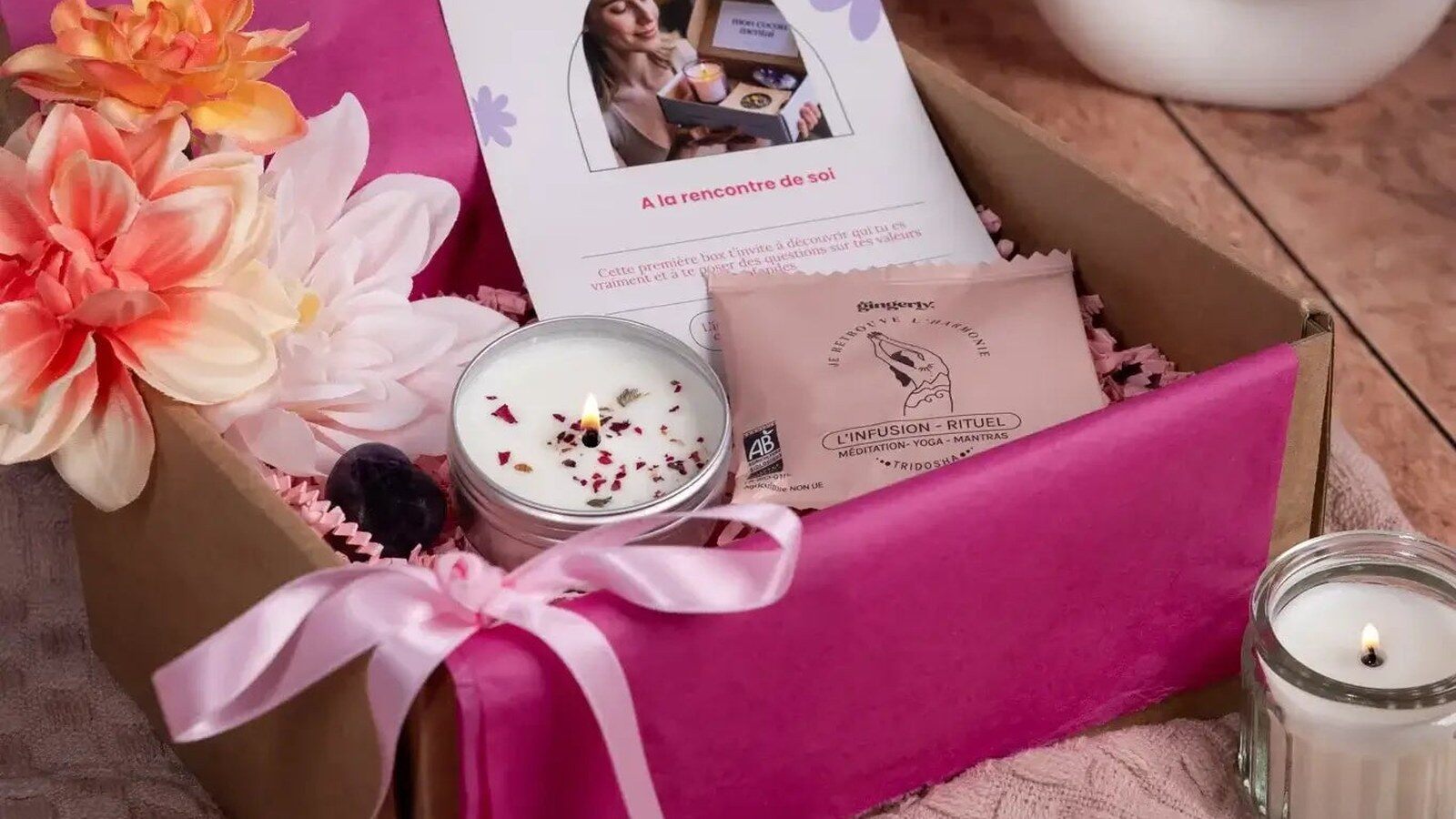 Une box Mon Cocon Mental ouverte avec un livret, une bougie, un sachet d’infusion et une pierre, dans un papier de soie rose